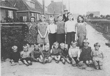 <p>Foto van een groep kinderen in de Worth Rhedenseweg, waarop aan de linkerkant een deel van het complex te zien is. De voortuinafscheidingen worden gevormd door lage heggen (Bron: Gelders Archief). </p>
